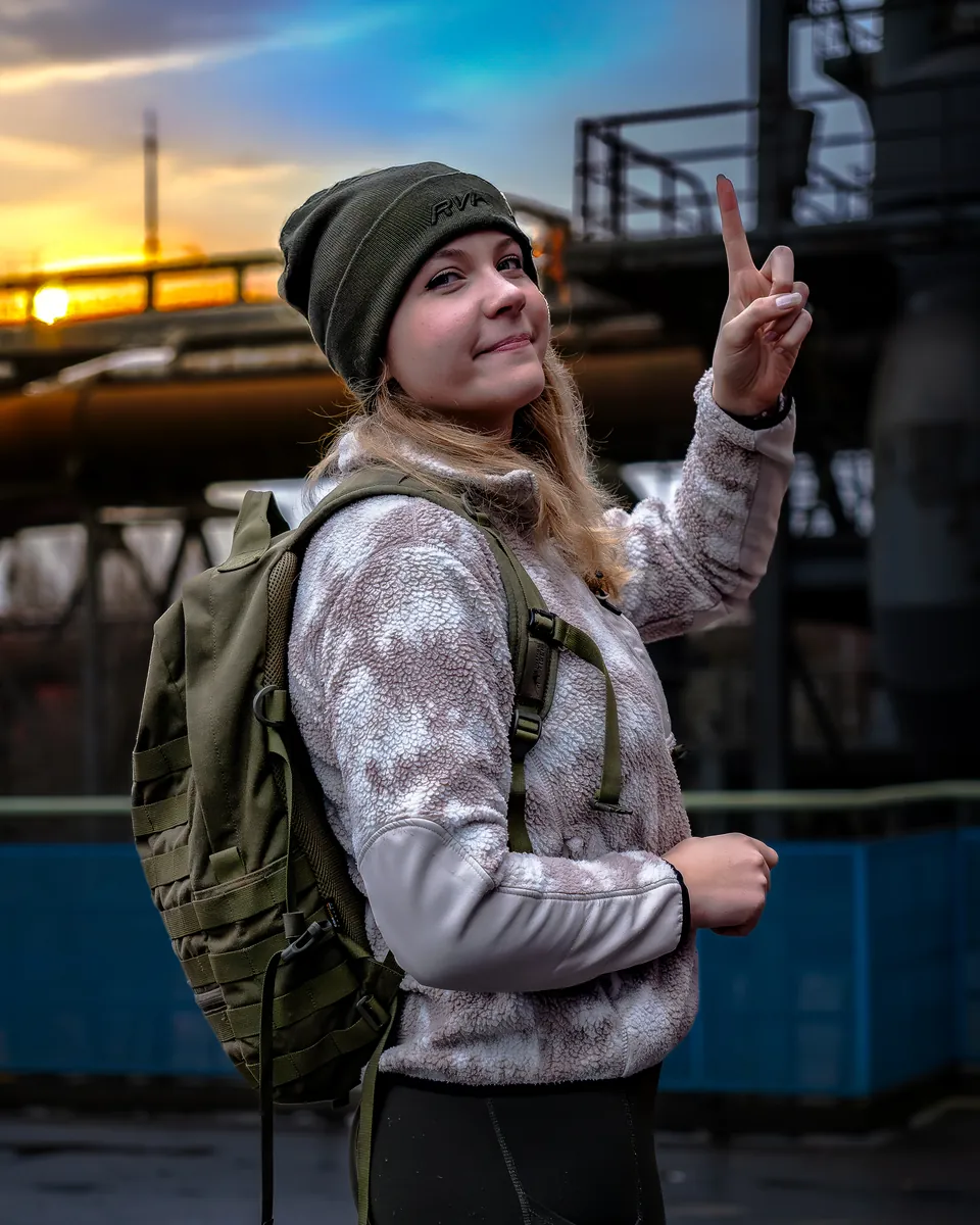 Frau mit Rucksack zeigt das Peace-Zeichen im Sonnenuntergang